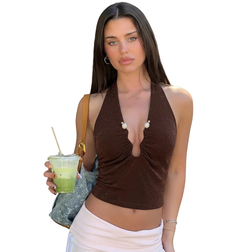 Woman in a brown halter top and white skirt holding a drink on a sidewalk.