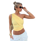 Woman wearing a yellow one-shoulder top and white pants outdoors.