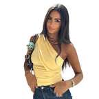 Woman in a yellow top and blue jeans standing against a stone wall with classical architecture in the background.