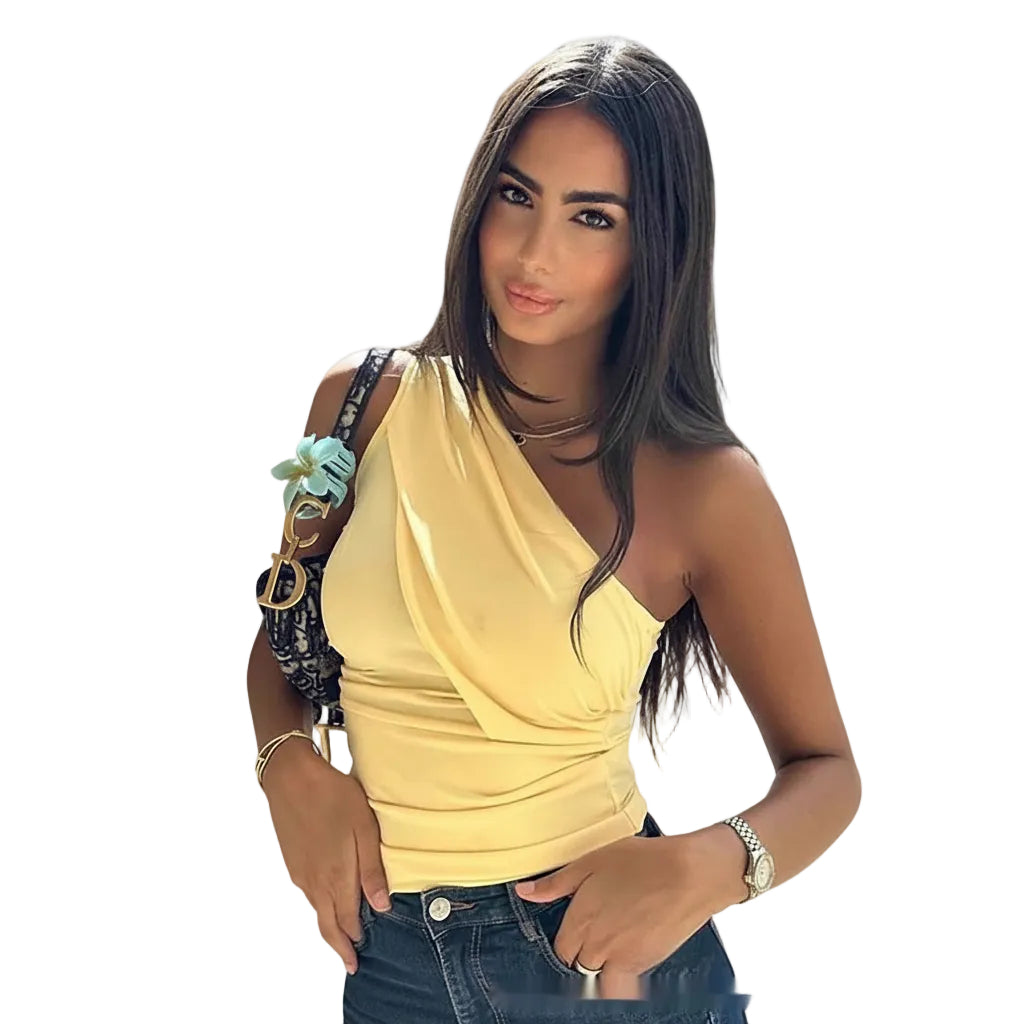 Woman in a yellow top and blue jeans standing against a stone wall with classical architecture in the background.